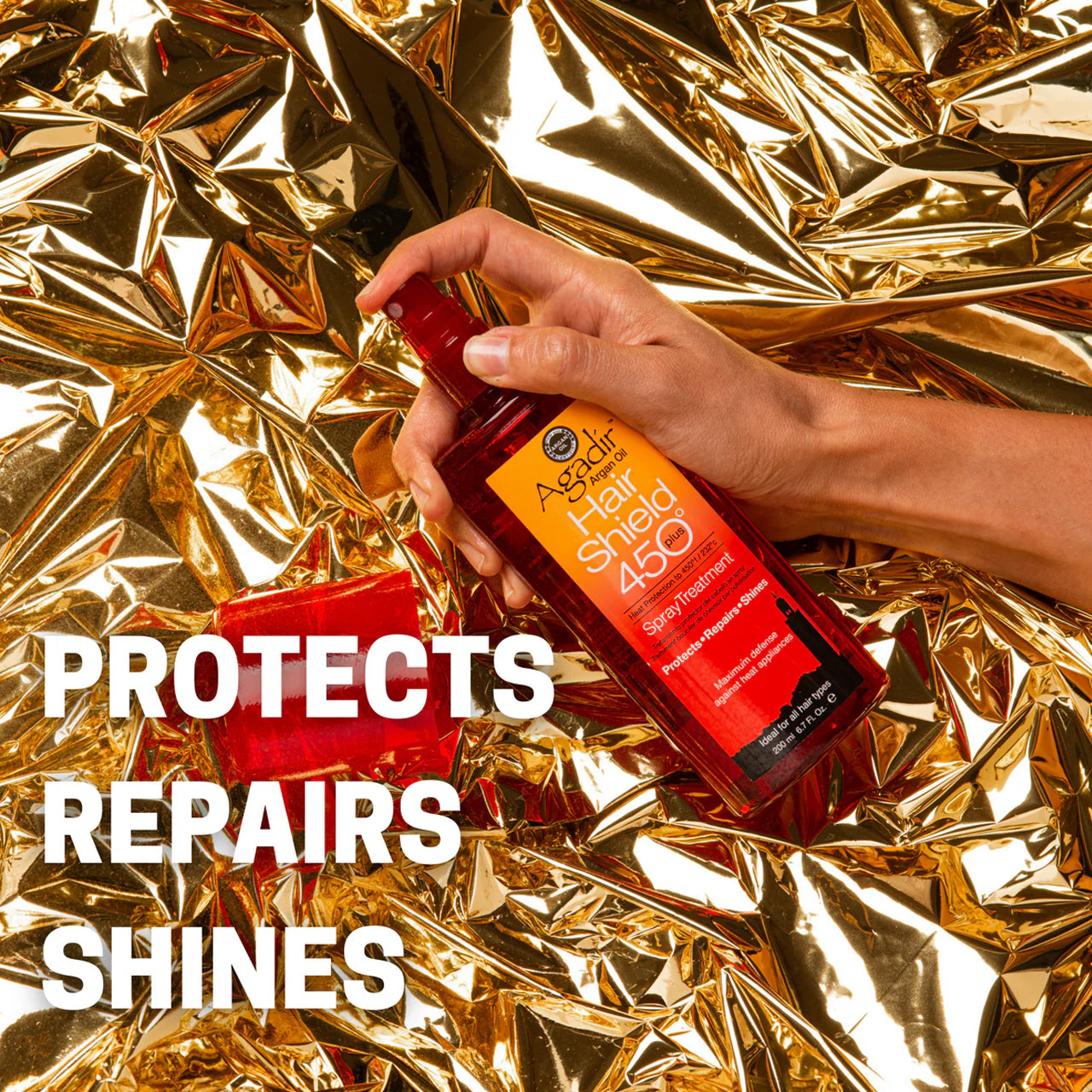 Agadir Hair Shield 450 Plus Spray bottle next to argan nuts and oil, highlighting natural ingredients.